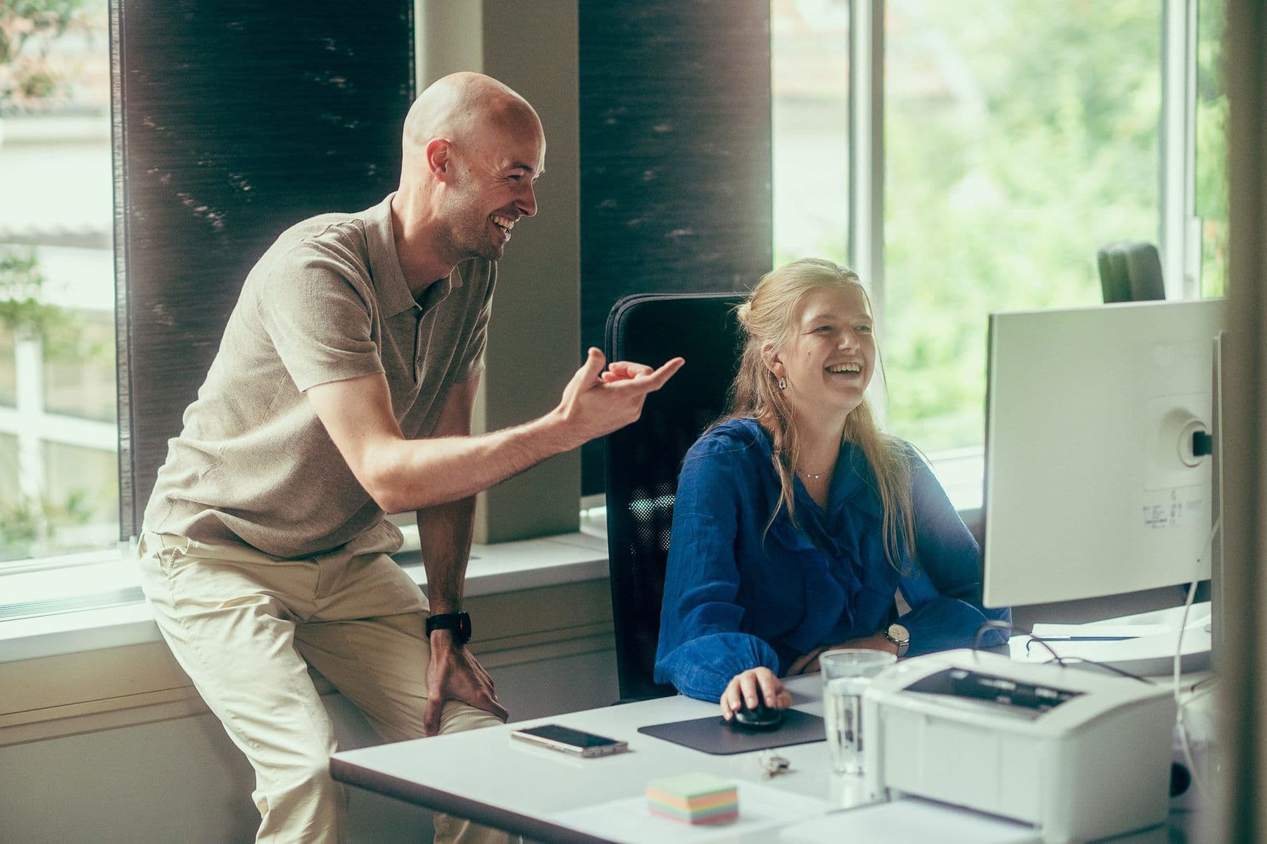 Twee collega's lachen samen om iets op het scherm van een computer