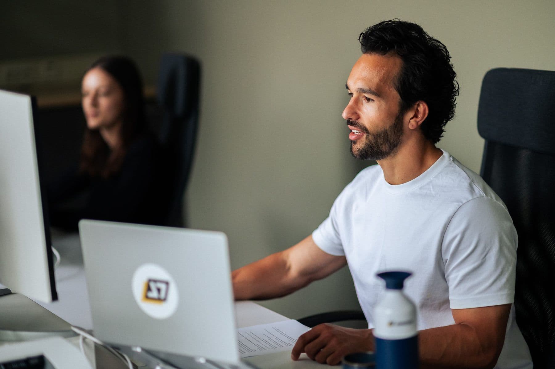 Een collega aan zijn laptop met het JoinSeven-logo op een sticker, op de achtergrond een collega