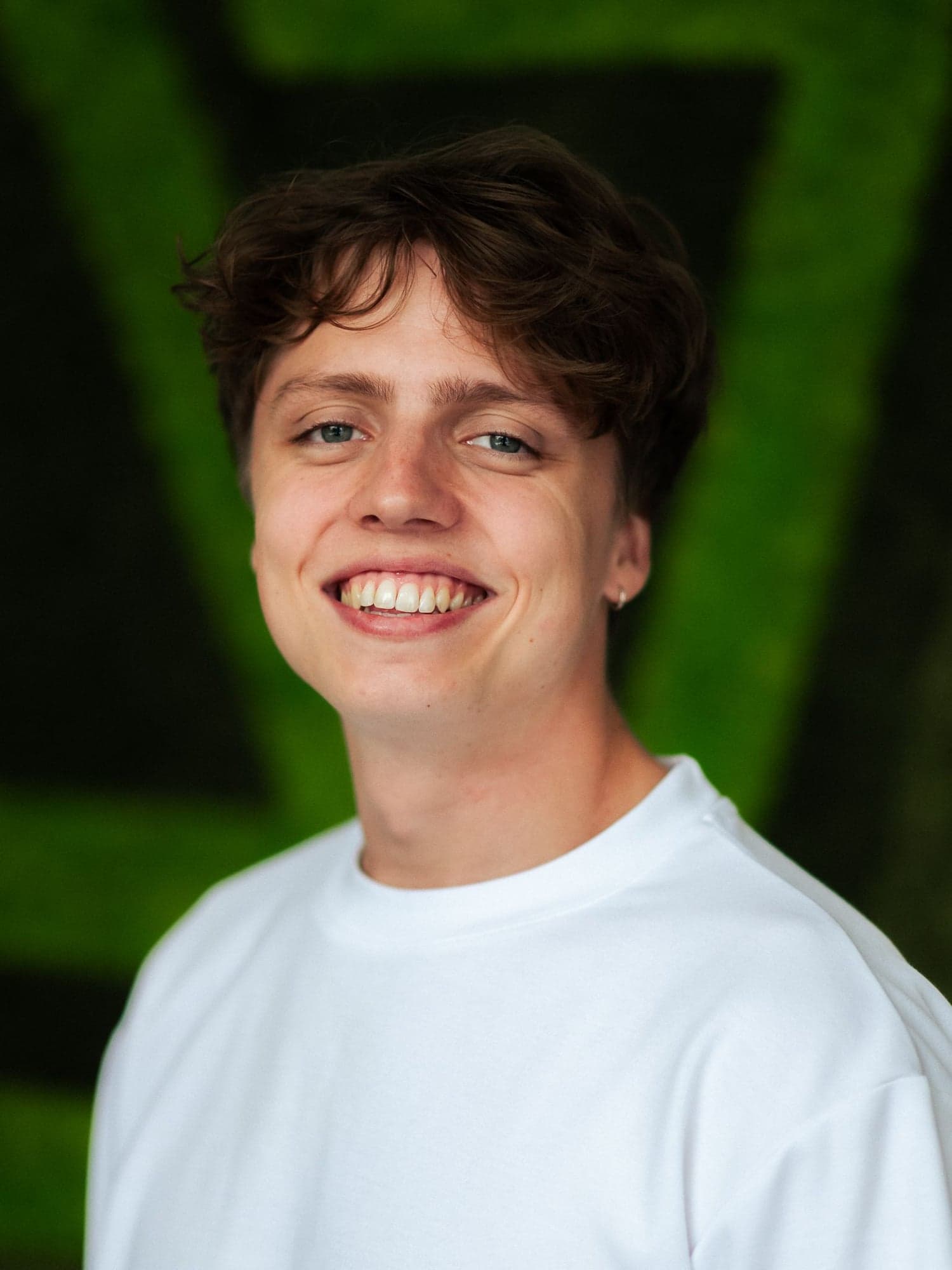 Portret van Daniël Vink, lachend in een wit T-shirt voor een groene mosmuur