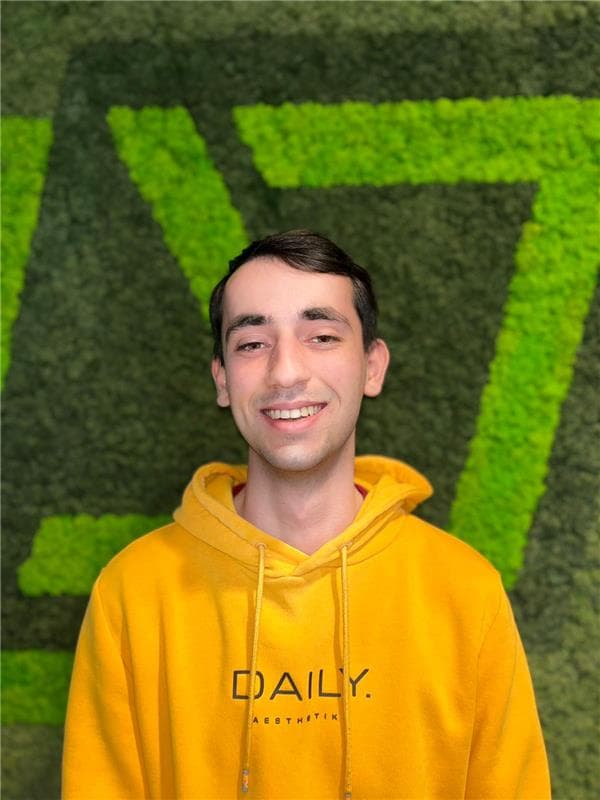 Portret van Marten Fleuren in een gele hoodie voor een groene mosmuur