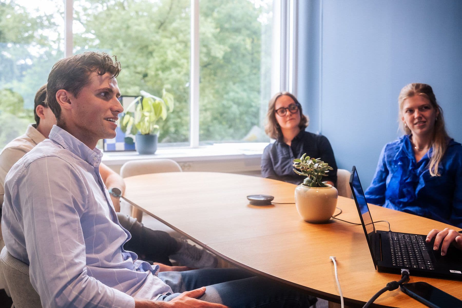 Drie collega's in gesprek aan een ronde tafel met een laptop