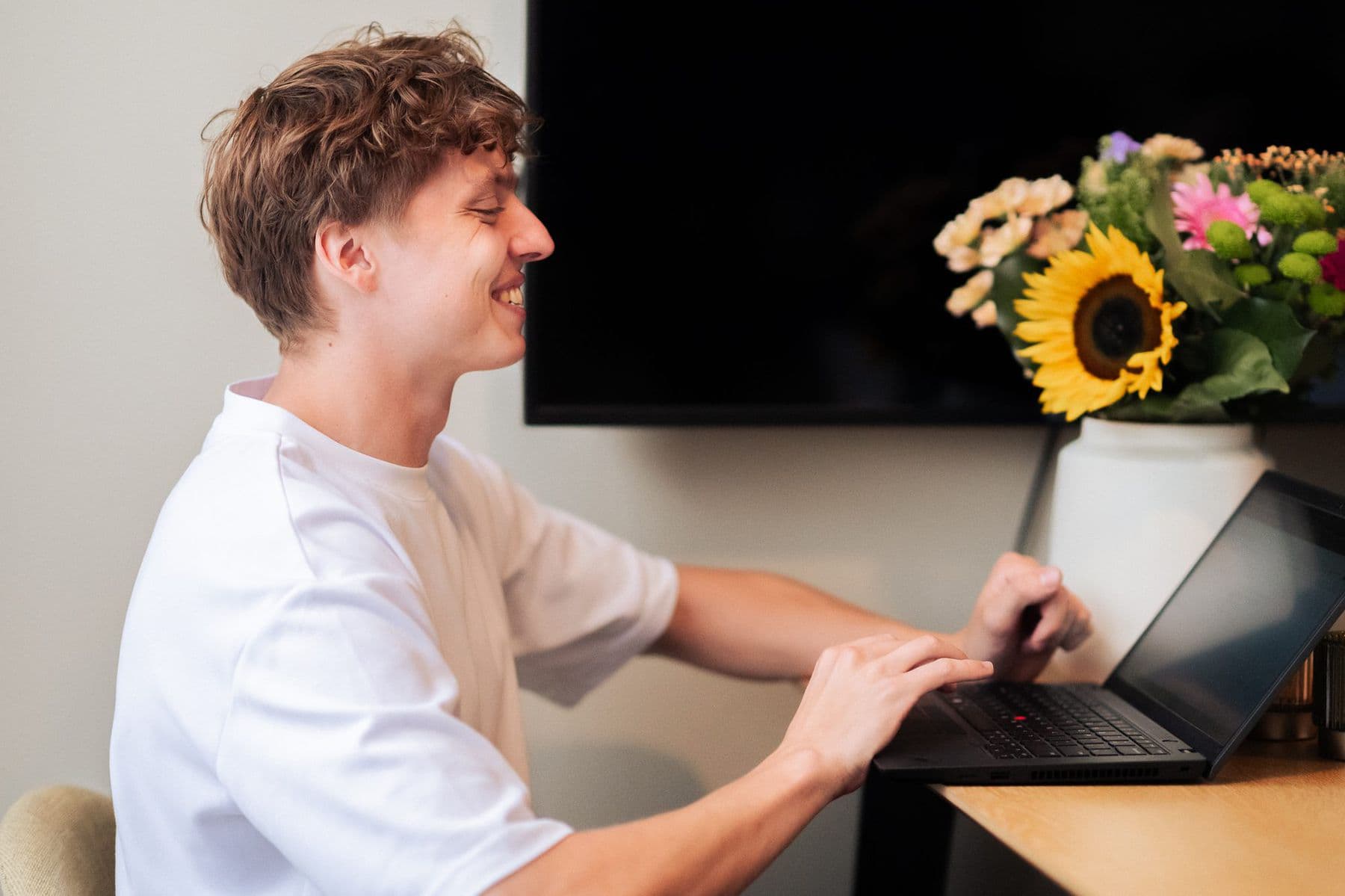 Een collega werkt glimlachend op zijn laptop, naast een boeket bloemen