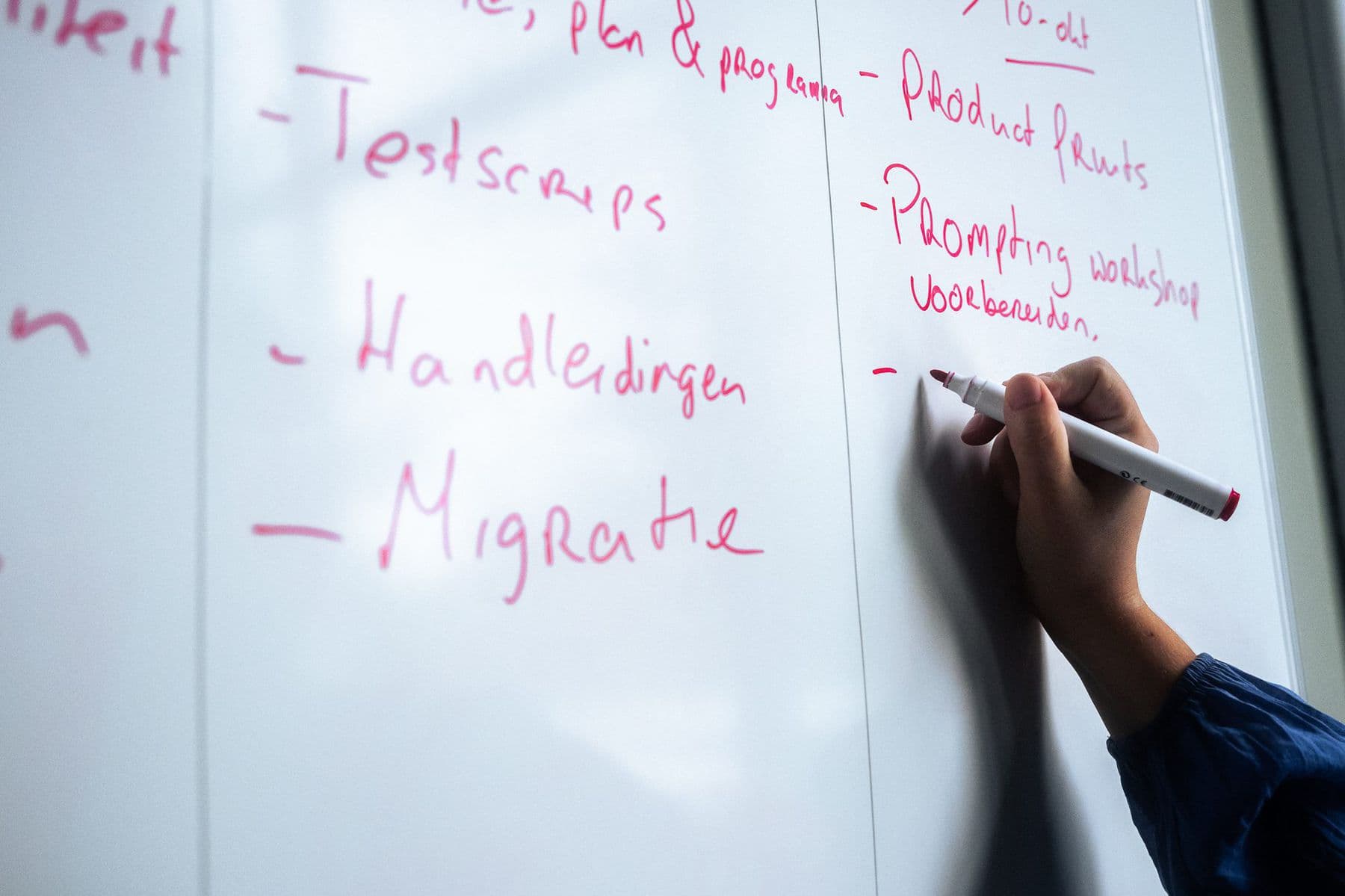 Een hand schrijft met een stift stappen op een whiteboard, waaronder testscripts, handleidingen en migratie