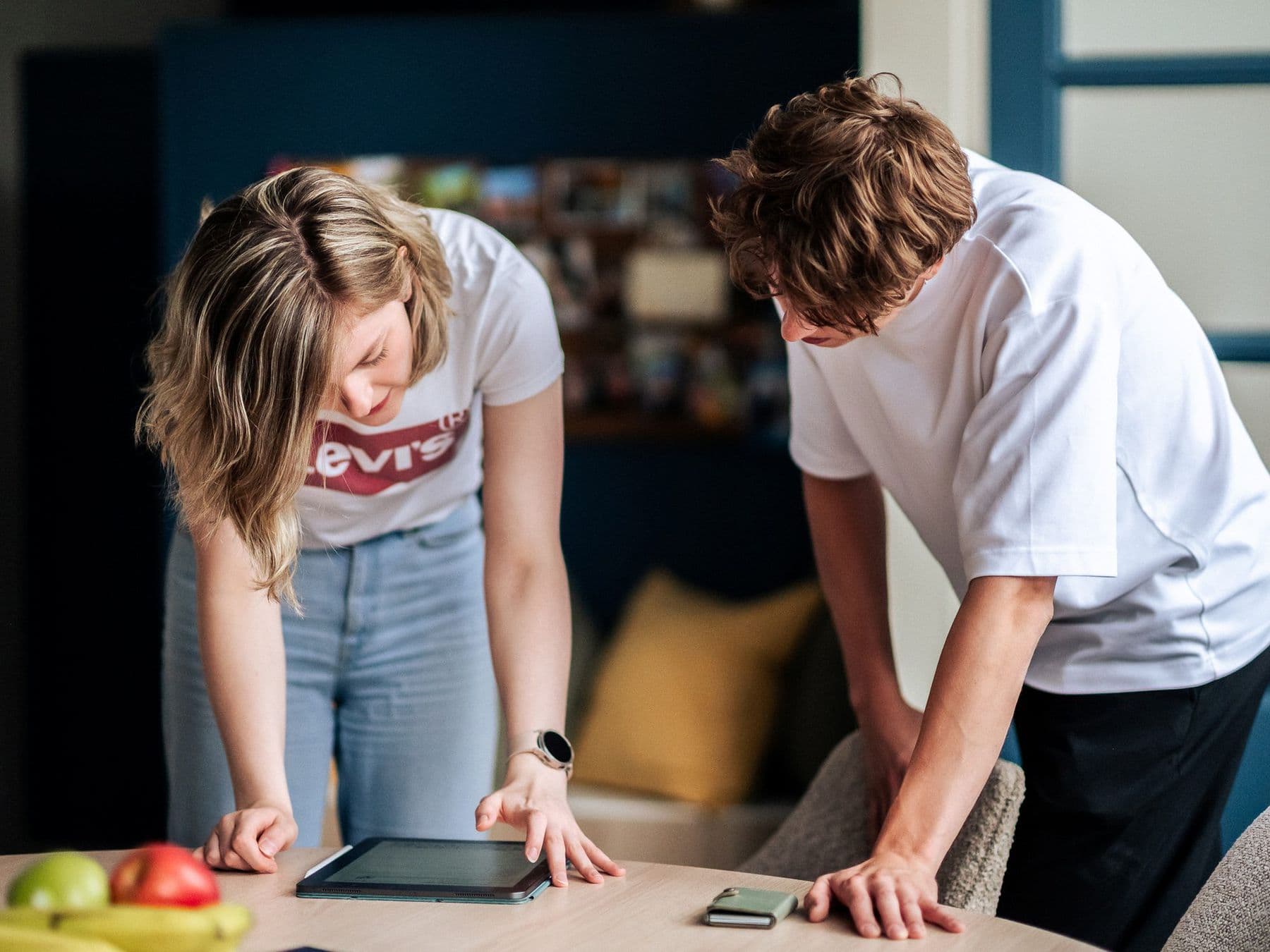 Twee collega's staan over een tafel gebogen en kijken samen naar een tablet